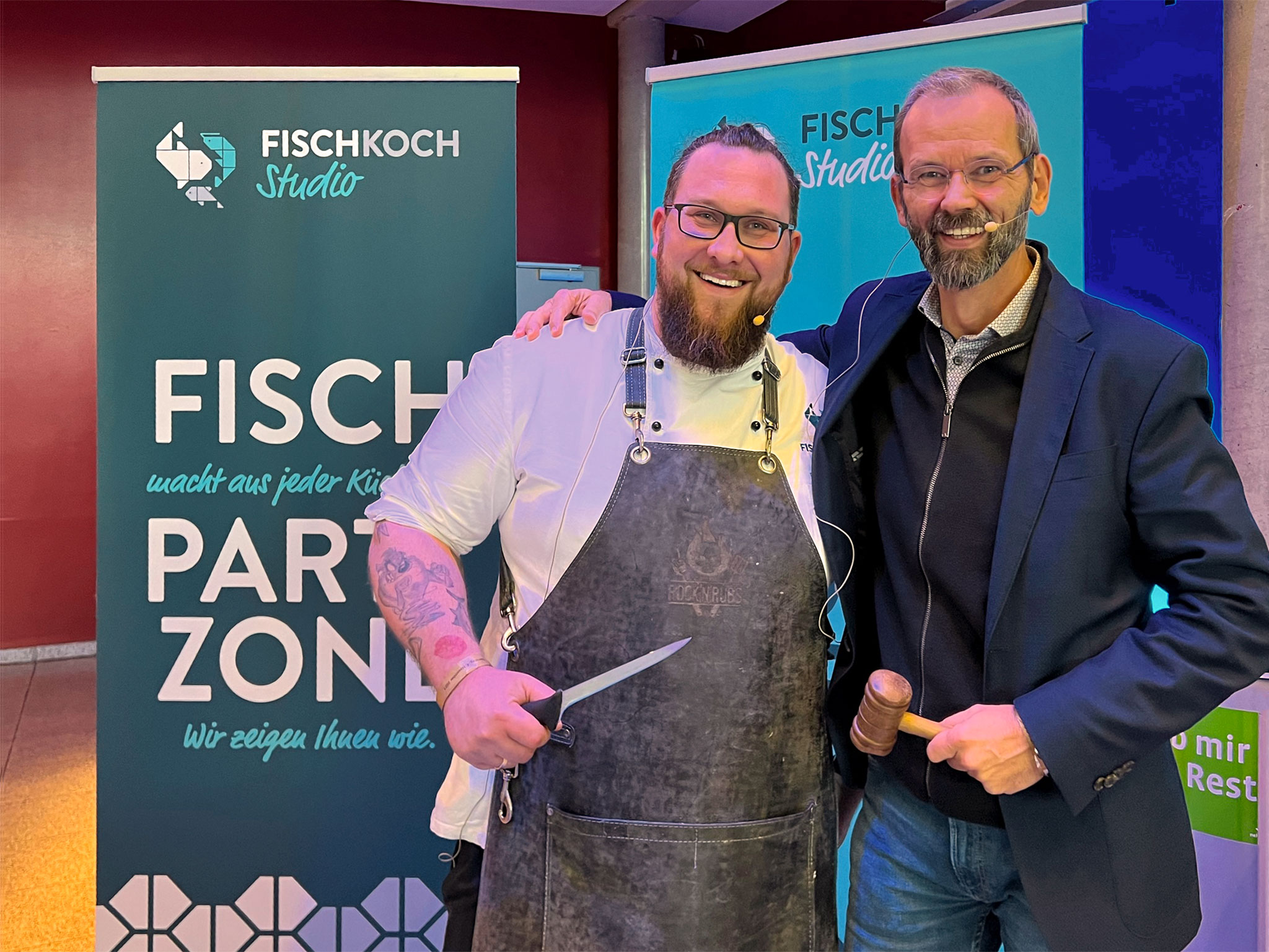 Impressionen von einer vergangenen Fischparty: Zwei männliche Protagonisten posieren fürs Foto während einer Fischauktion