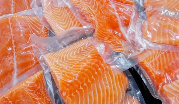 Ein Haufen frischer Lachsfilets, in Kunststofffolie vakuumiert auf einer schwarzen Tischplatte